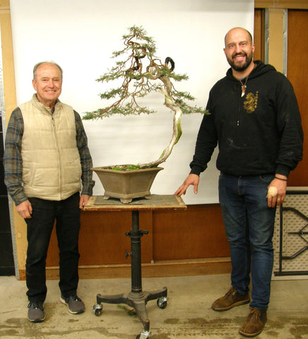 Dave De Groot standing in a vest beside Mauro Stemberger with a bonsai tree between them