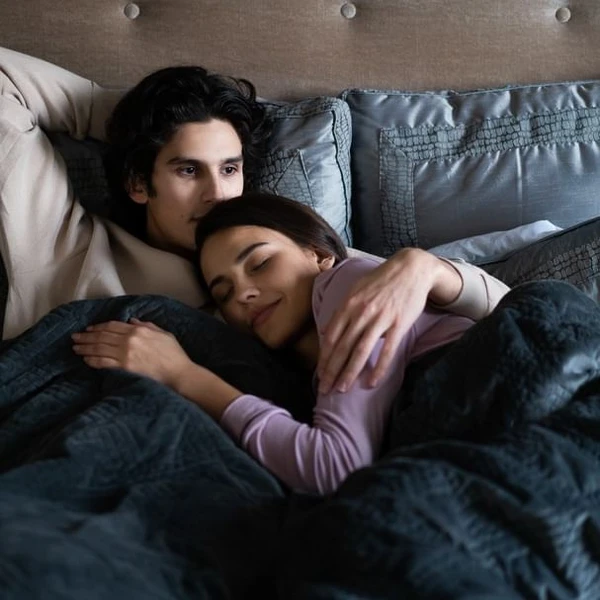 Man lying in bed with his arm wrapped around a girl sleeping on his chest