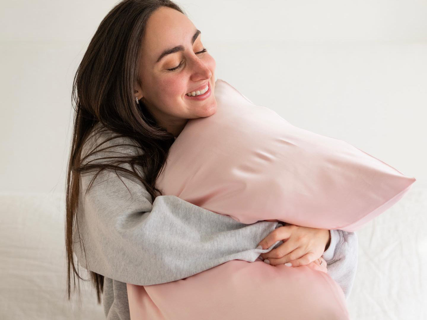 A beautiful, young woman happily hugging a pillow fitted with Hush Silk Pillowcase in pink color.