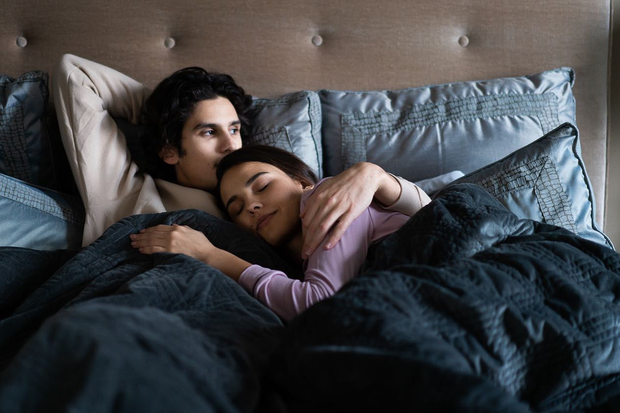 A couple lovingly cuddling in bed while covered in a grey Hush Classic Weighted Blanket.