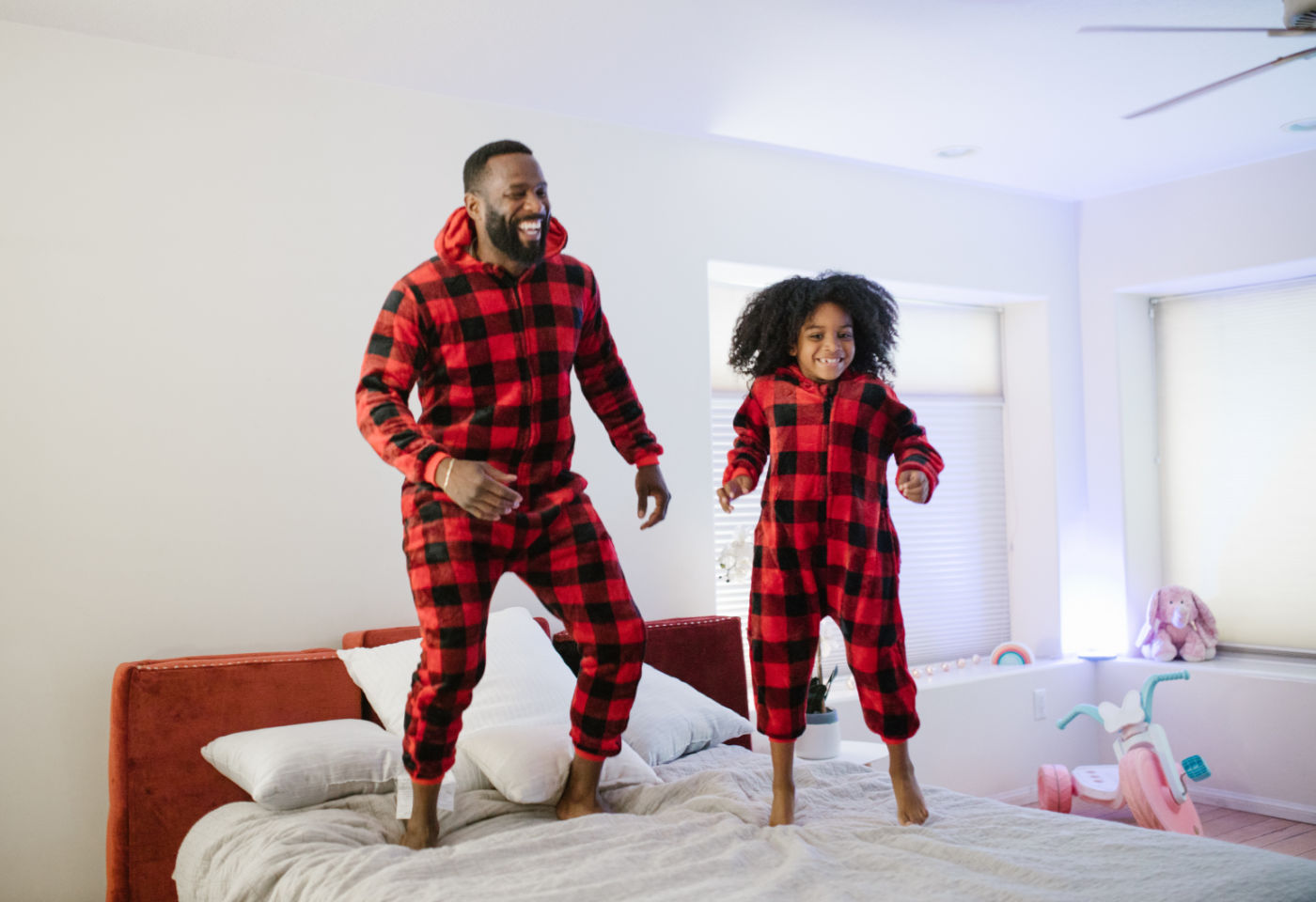 father and daughter wearing red plaid pajamas and jumping on bed