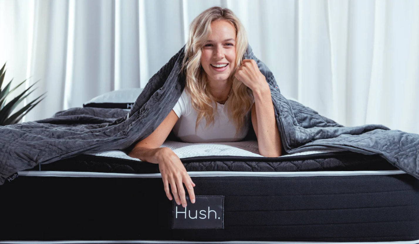 smiling woman lying on her stomach on a Hush mattress and happily covered with blanket