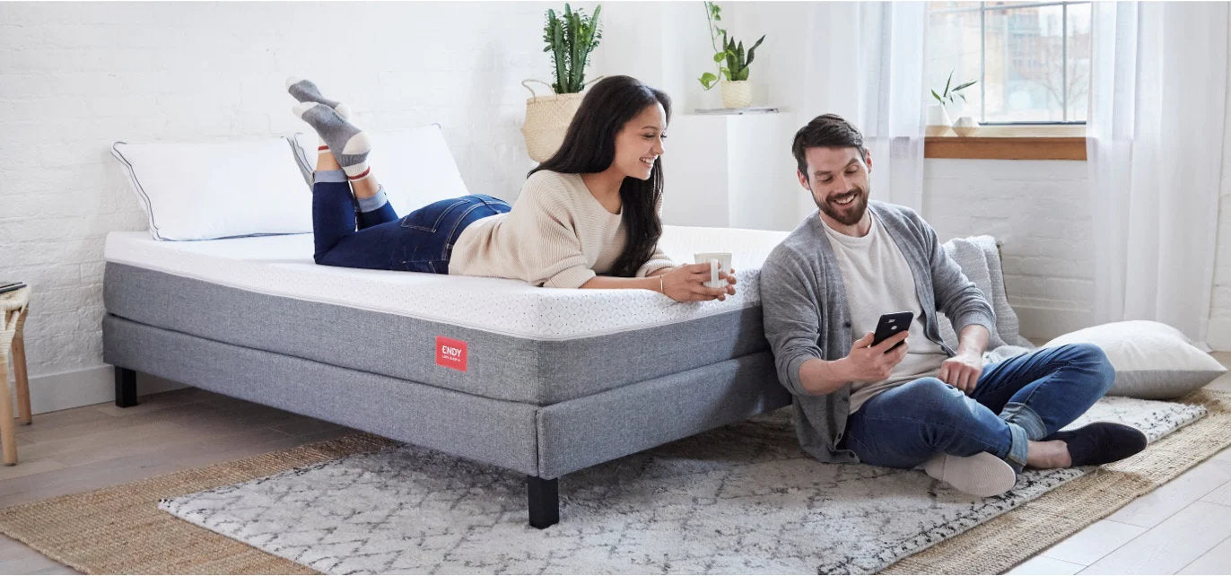 woman lying on her stomach on an Endy mattress looking at a smartphone held by a smiling man sitting on the floor