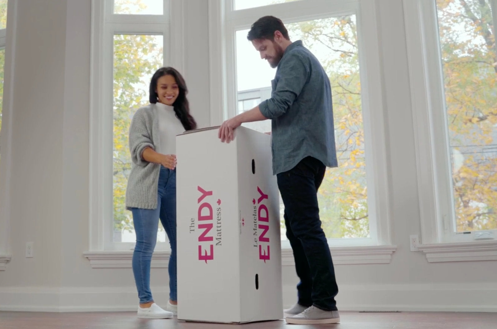 couple about to unbox an Endy Mattress on a white bedroom with big windows behind them