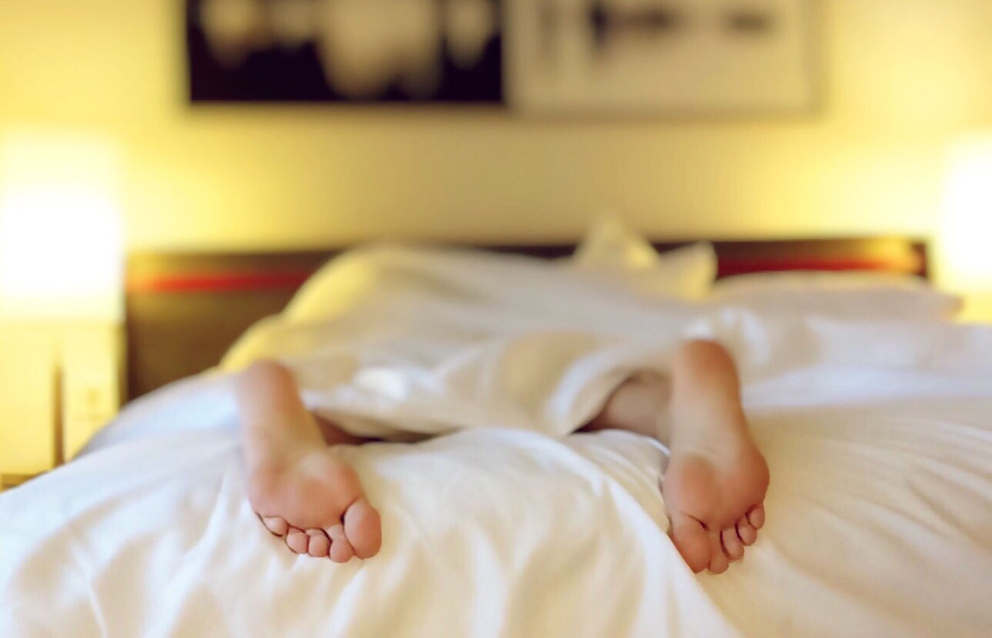 sleeping person covered with white sheets with tired feet hanging at the edge of bed