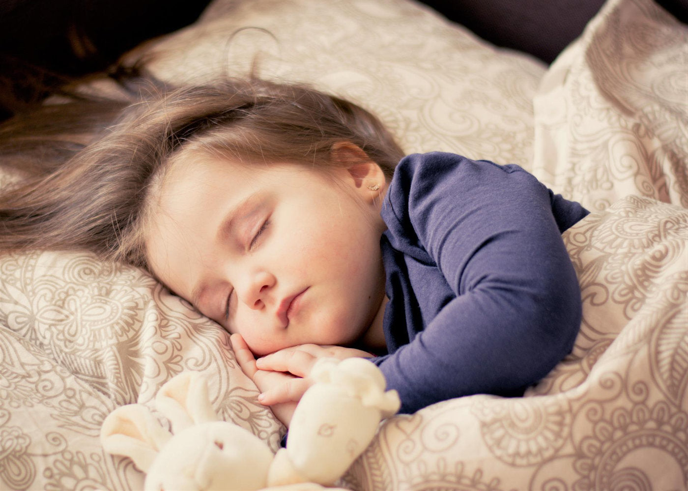 baby girl tucked in bed sleeping with a stuff toy