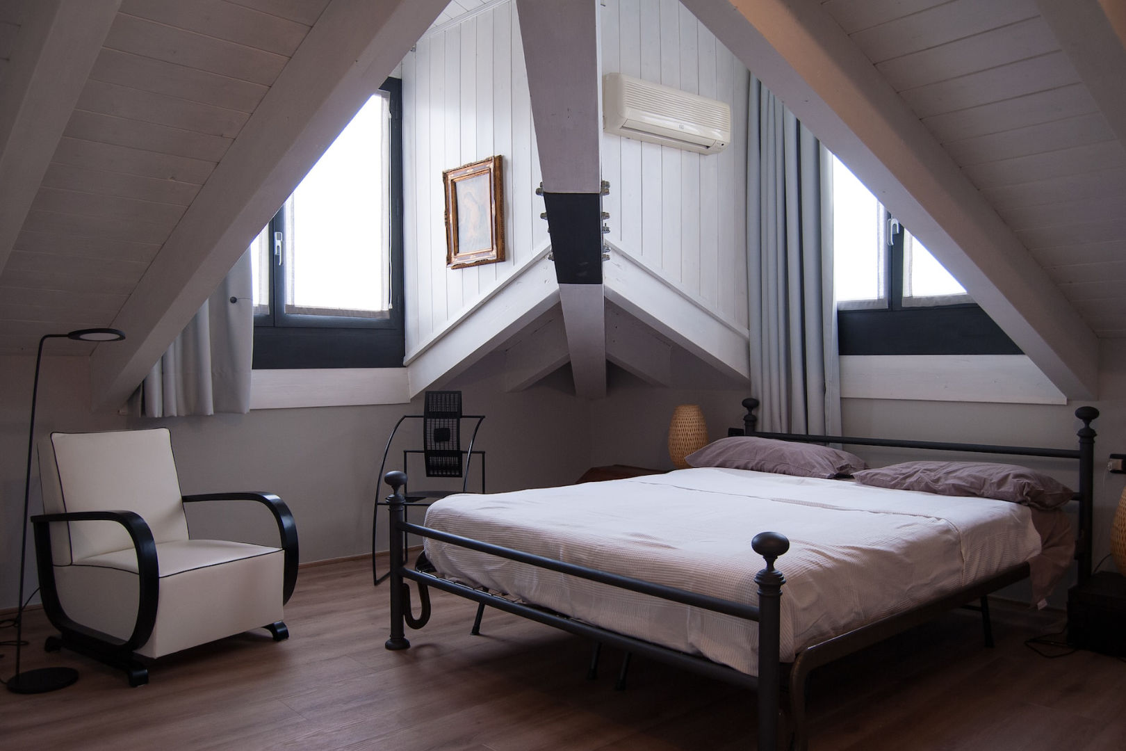 An attic bedroom with a black steel bed frame near a window.