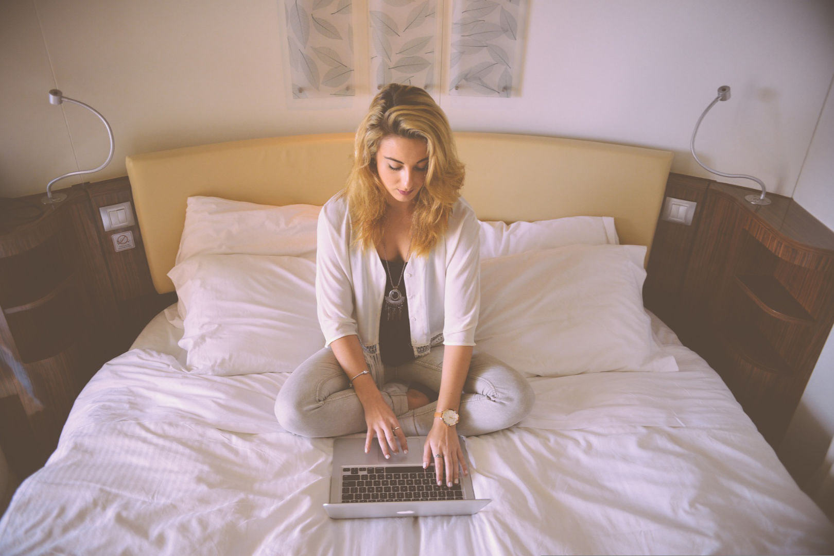 A woman working in bed sitting while typing on her laptop.