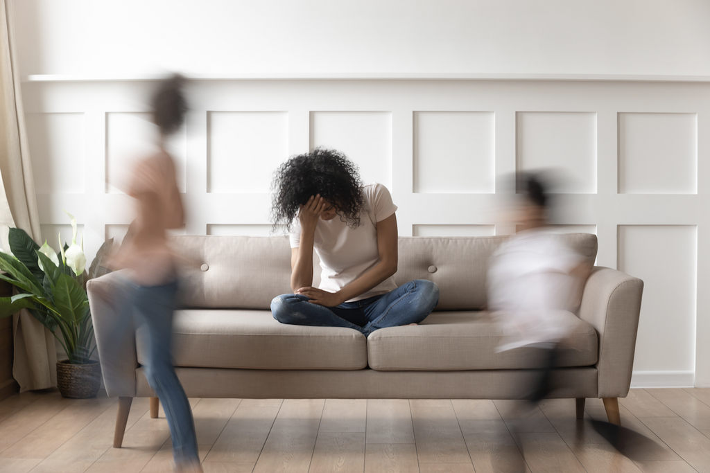 weighted blanket for ADHD: Stressed woman sitting on the couch with blurred images of children playing