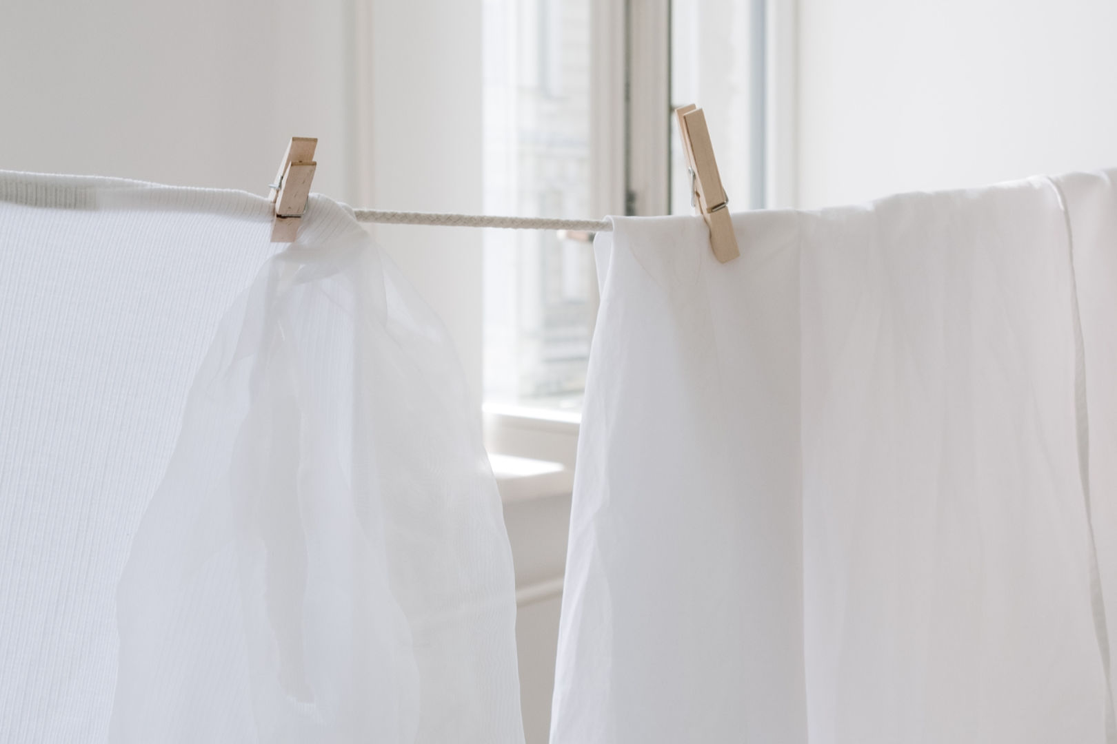 Clean white linens hanged in a clothes line pinned using natural bamboo clothespins.