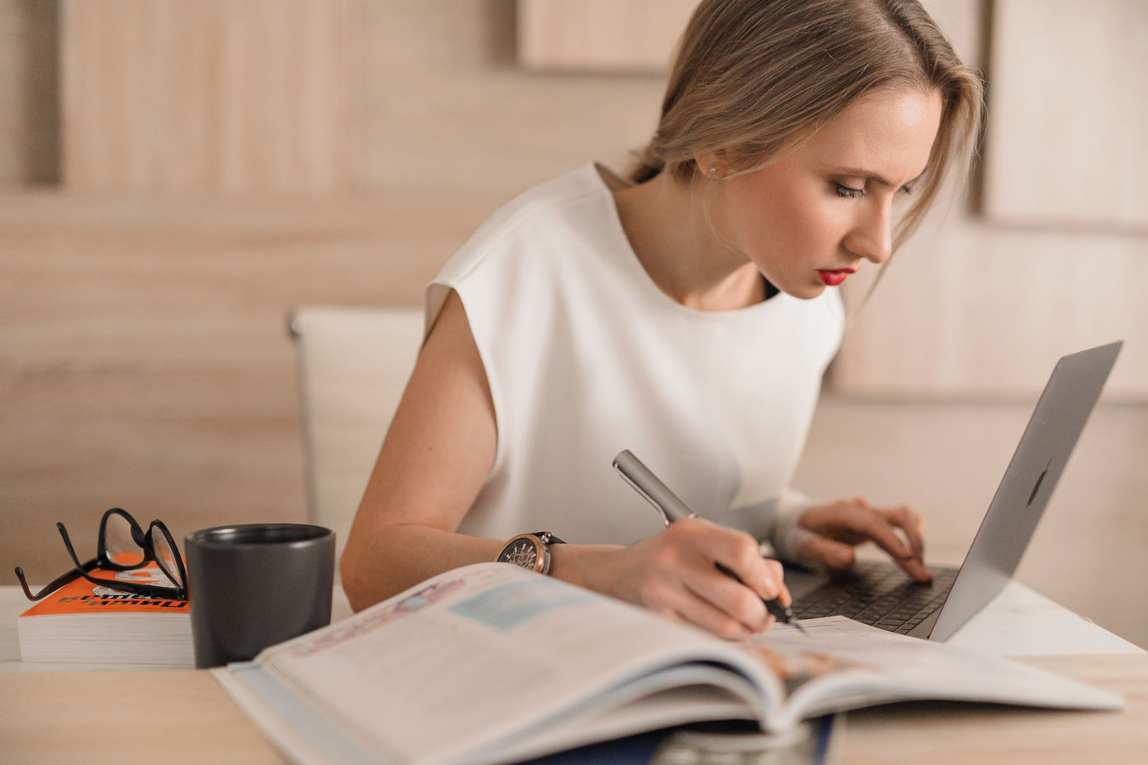 A young woman busy working on her laptop with a mug and opened books on her desk.