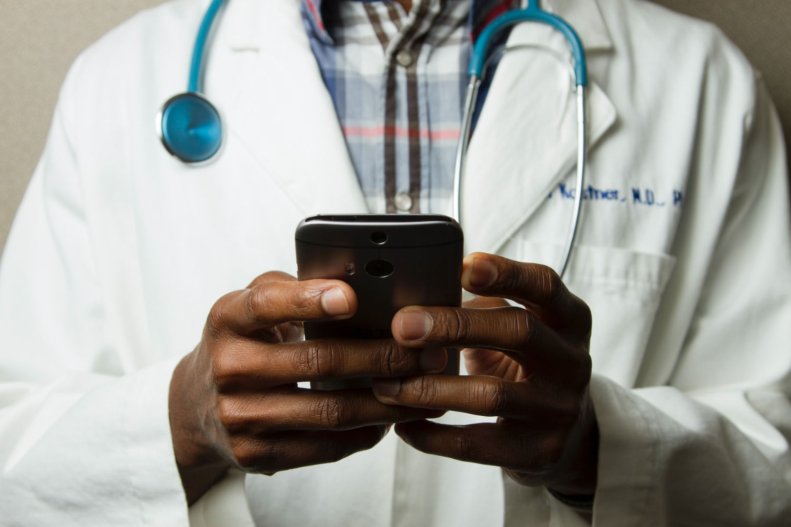 A doctor holding a cell phone with a green stethoscope on his neck.