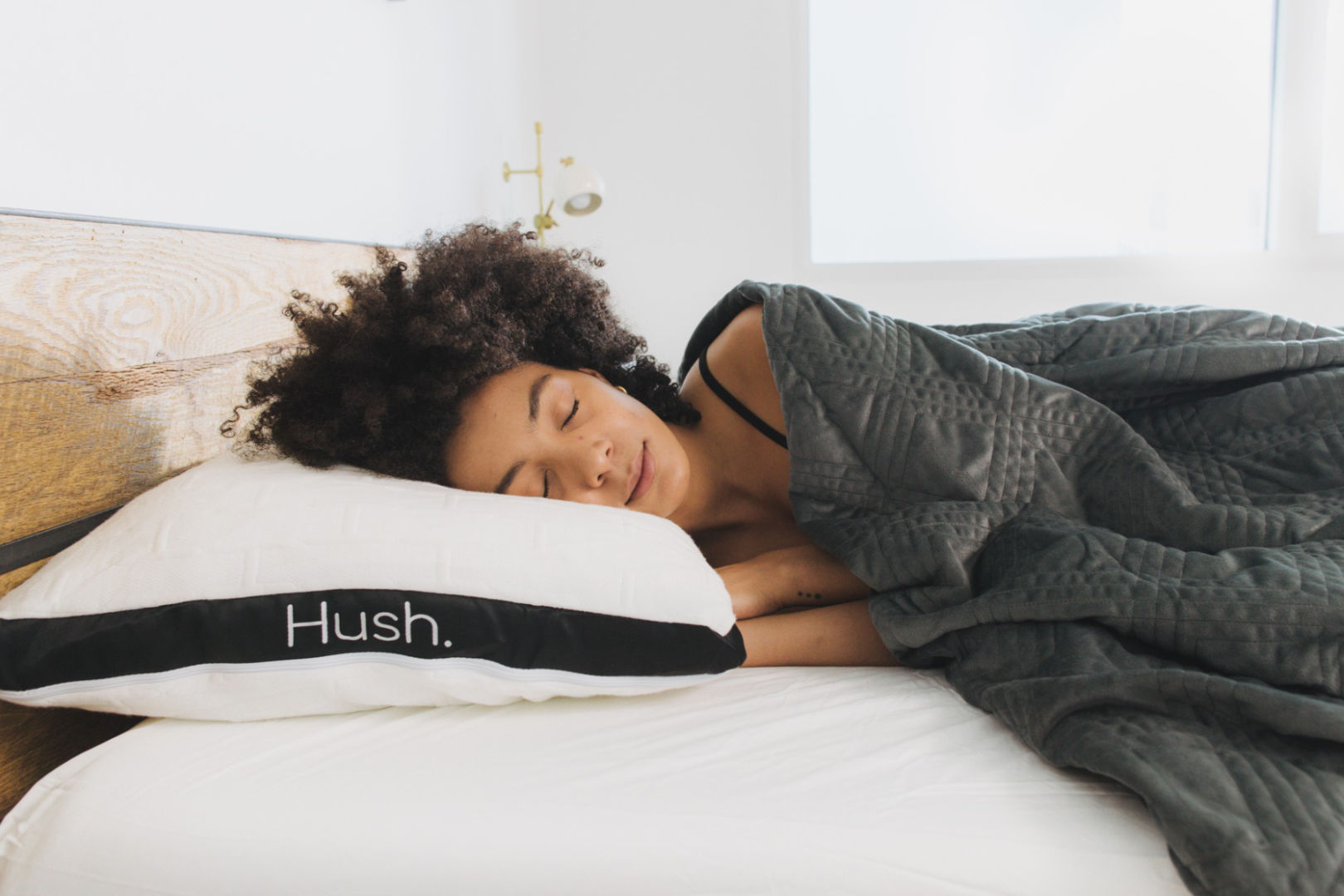 A young black woman sleeps peacefully with a Hush weighted blanket and Hush pillow.
