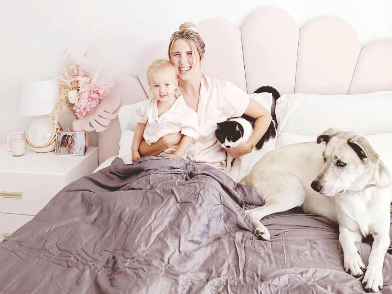 A mother smiling with a cat, dog and child on a bed together