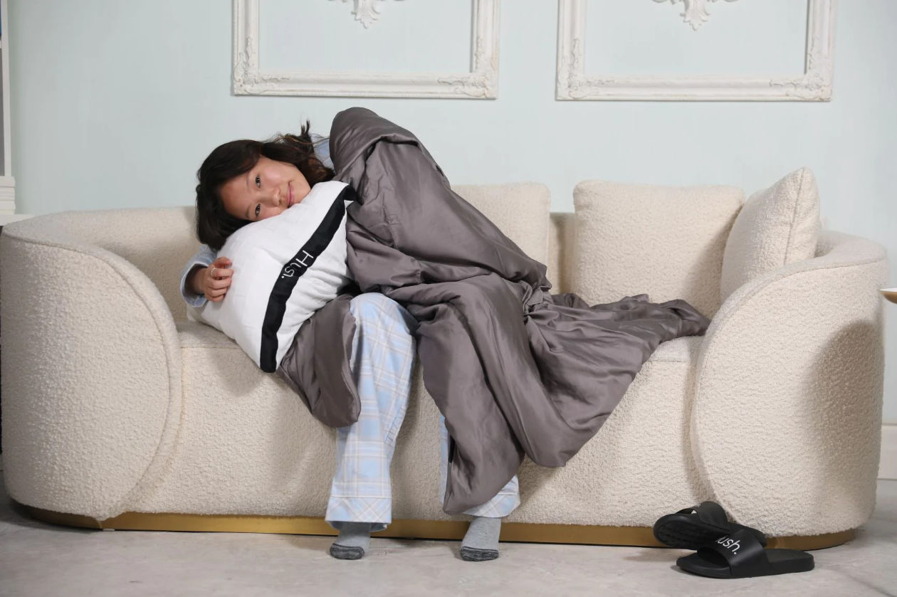 Woman covered with a Hush blanket and hugging a Hush pillow