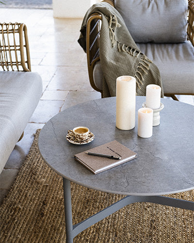 Close up of Cane-line Twist coffee table with a marble look table top, a cup of espresso, stearin light, plaid on the lounge chair