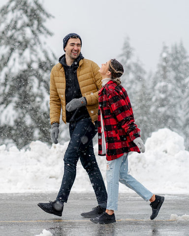 A man and a woman walking through a snowy city wearing waterproof shoes.