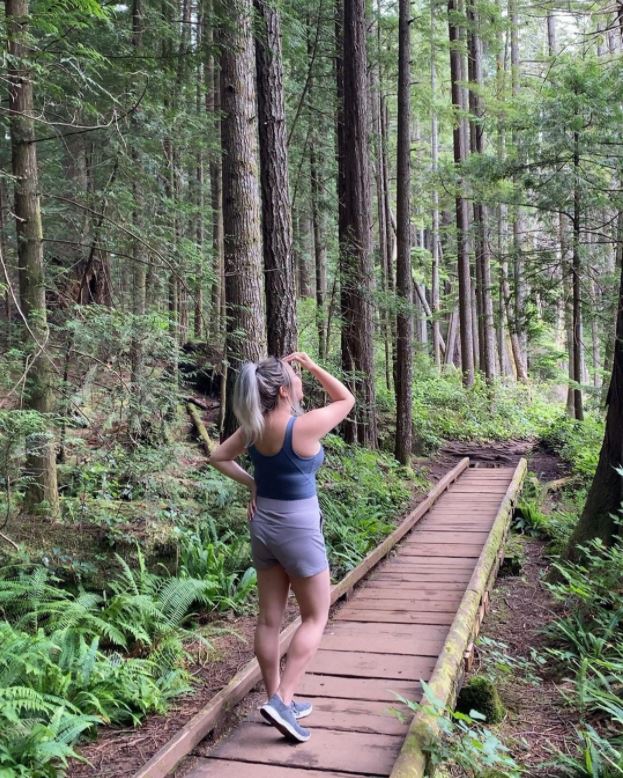 A woman walking along a path in the forest while wearing workout clothes and comfortable waterproof shoes