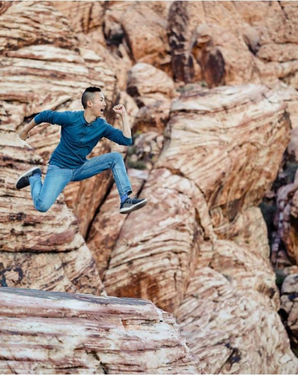 A happy man jumping across giant red rocks while wearing his Vessi Charcoal Grey Cityscapes
