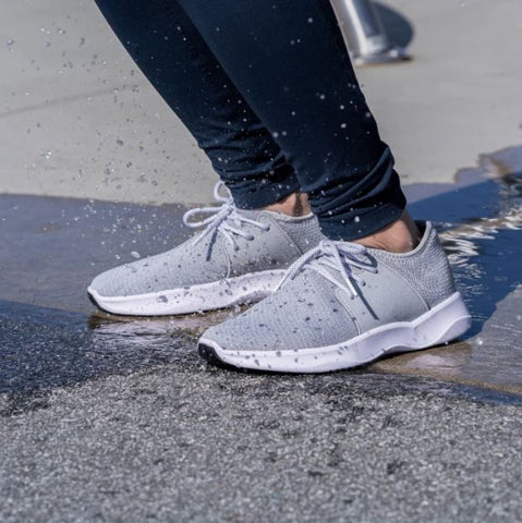 A close up shot of a woman’s Vessi waterproof walking shoes splashing in puddles on pavement