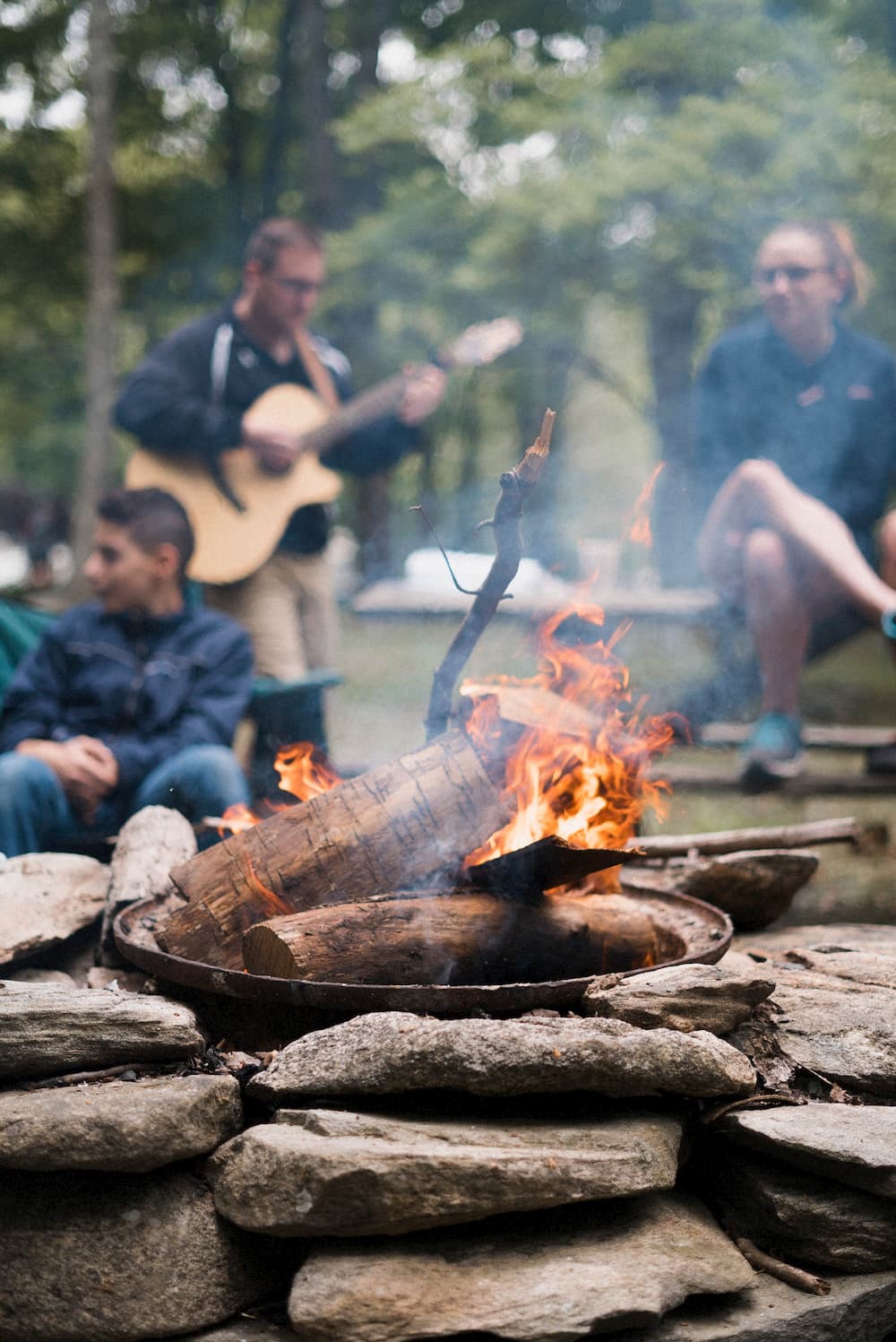 A group of friends gathered around a campfire, playing guitar and chatting