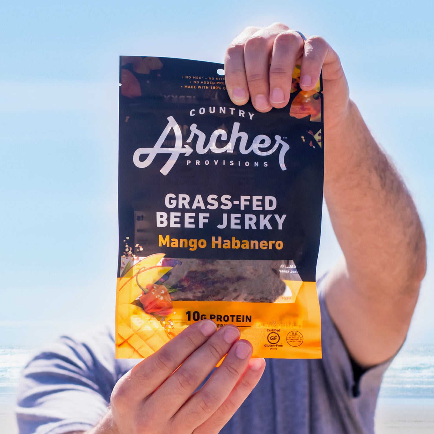 person holding a bag of Country Archer mango habanero jerky at the beach