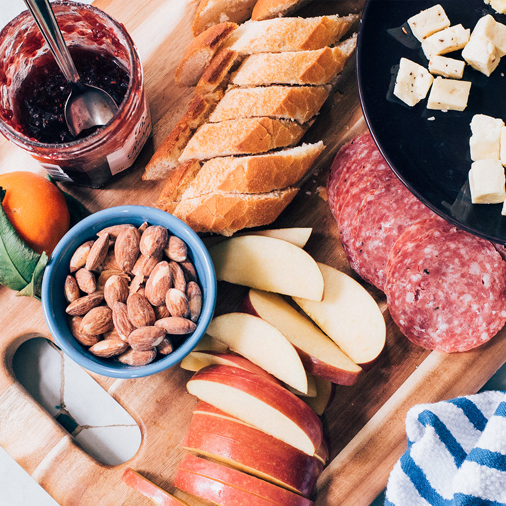 charcuterie board featuring bread, jam, almonds, apples, salami and cheese