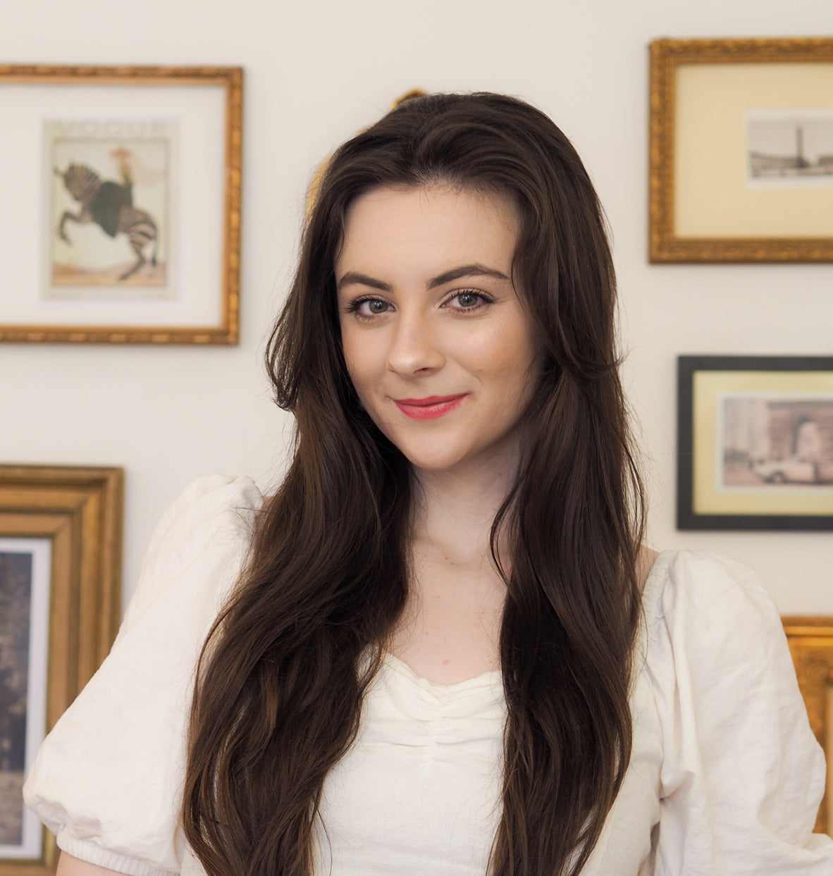 Emma Butler poses for the camera wearing a white blouse and her hair draped nicely over her shoulders.