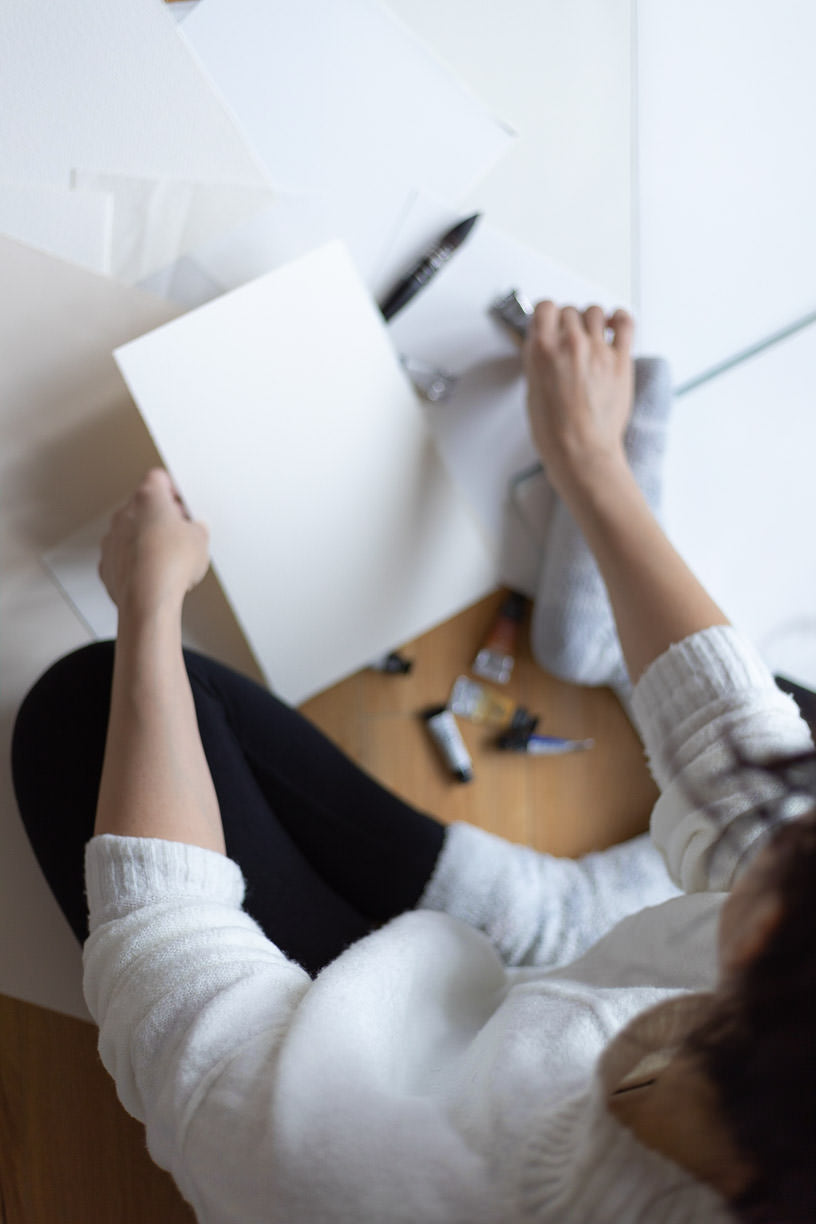 woman sitting on the floor with art supplies watercolor paper and brushes