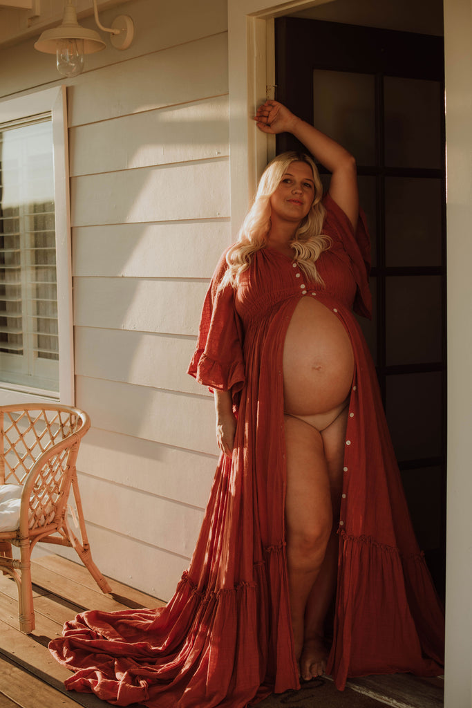 A beautiful pregnant lady wears Mama Rentals Reclamation Ruffle Me Open gown in rust colour at her maternity shoot,