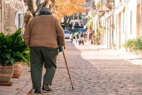 An older man walking down the street with a cane because he didn't find natural ways to protect against osteoporosis.