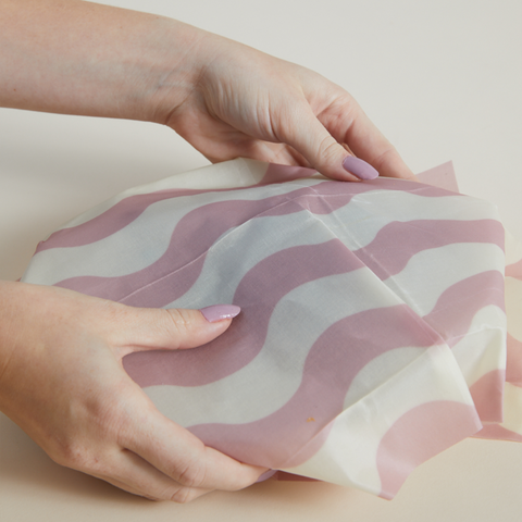 Hands wrapping plate in pink and white wavy striped beeswax wrap 
