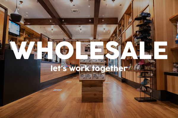 'Wholesale, let's work together' text overlaid on an image of a coffeeshop displaying our retail bags of coffee for sale.