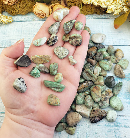 Hand holding collection of variscite stones. More of these specimens are in the background