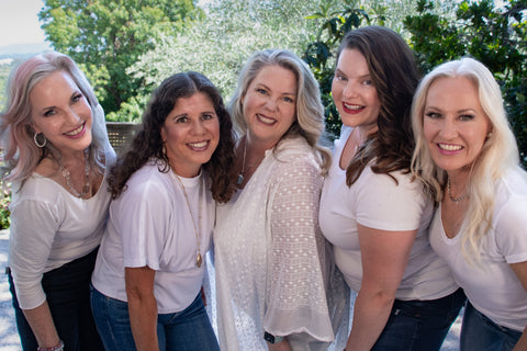 group of women over 50 leaning in wearing white shirts and pink lipstick.