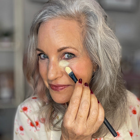 woman applying yellow concealer with brush.