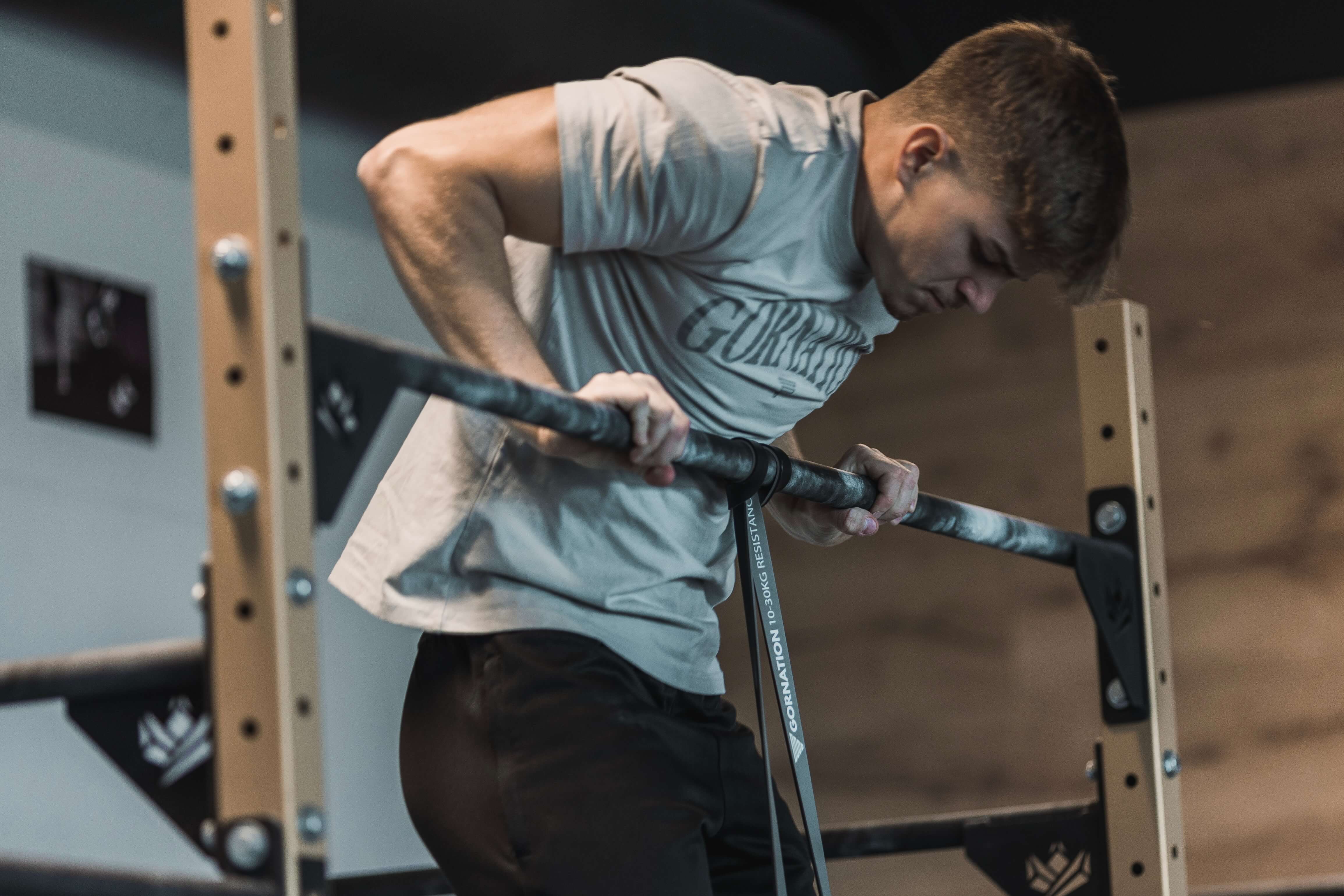 Calisthenics Athlete wearing a GORNATION T-Shirt performing a Muscle Up on a bar using a Resistance Band and Chalk by GORNATION