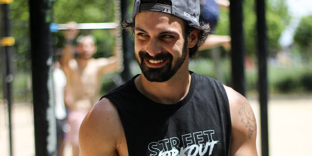 San Gohan smiling and wearing gornation cap and street workout tank top at a calisthenics workout park