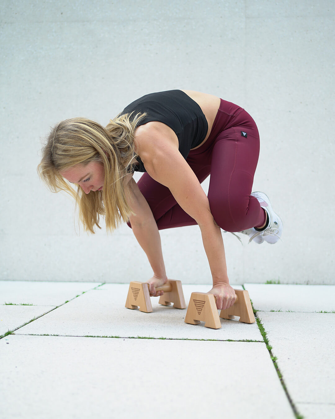 female calisthenics athlete doing a frog stand on wooden parallettes