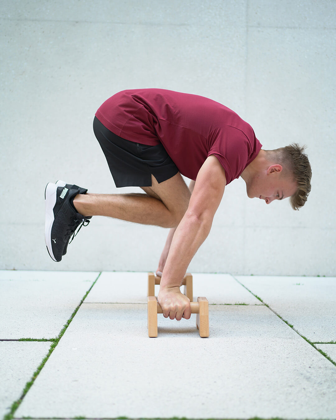 calisthenics athlete doing tucked planche on wooden parallettes by gornation