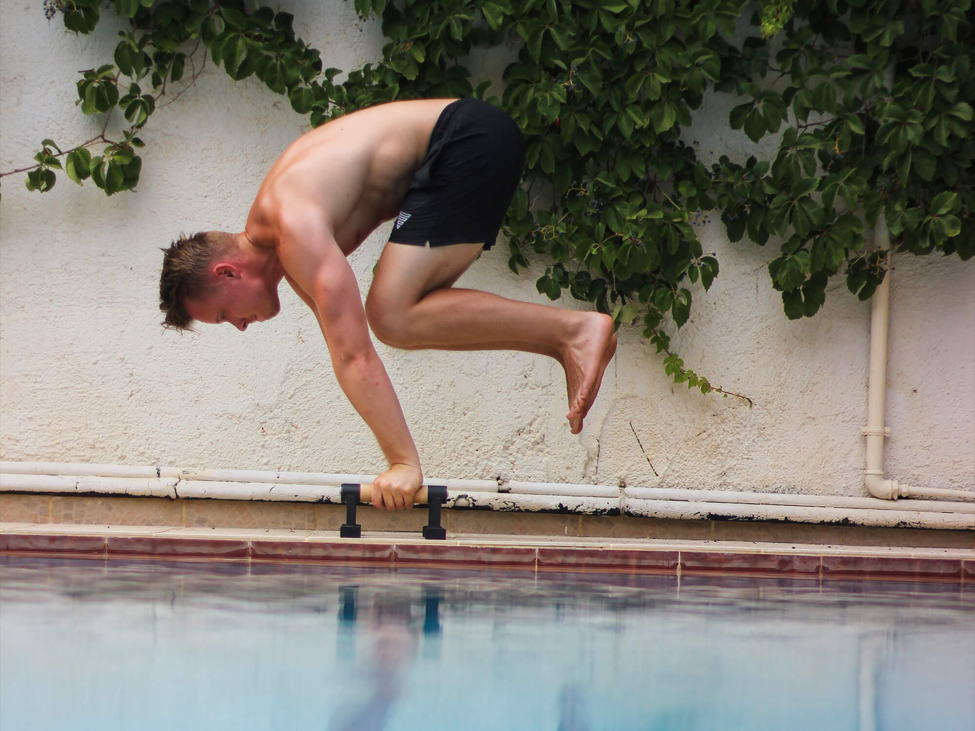 athlete holding a tucked planche on parallettes at the pool