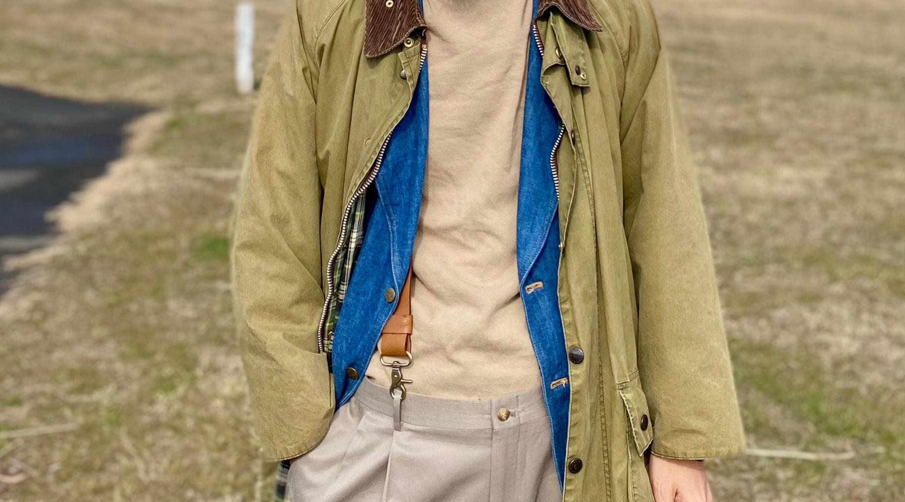 Image of layered clothes, a cream colored t-shirt with a blue denim jacket and an army green coat with a brown corduroy collar. A bit of camel leather suspenders is visible from under the jackets.