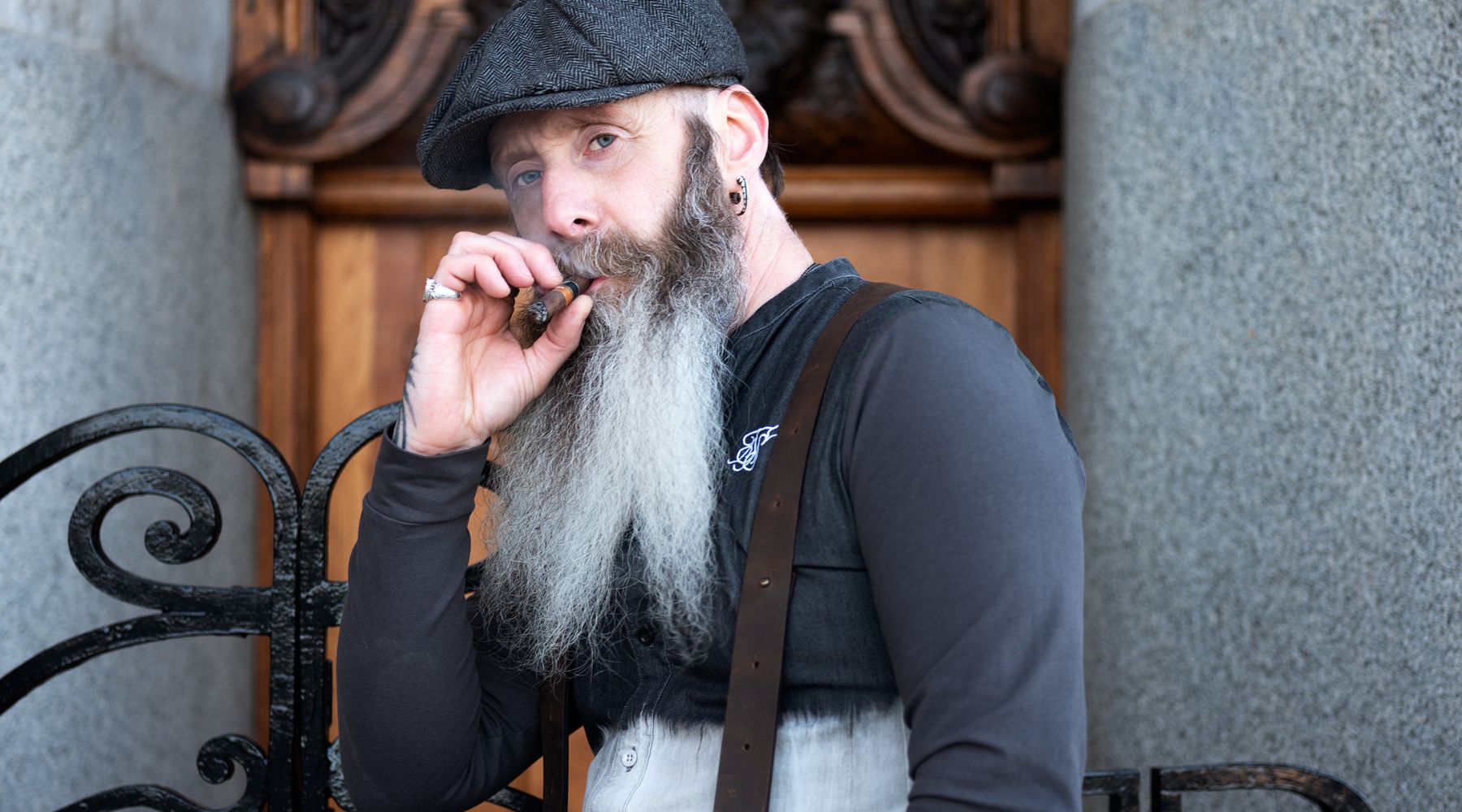 Homme avec barbe et casquette plate portant des bretelles originales en cuir marron foncé