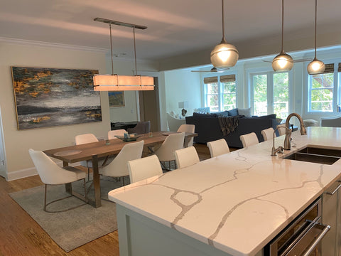 Bicycle Glass Arctic Swell 767 Single Pendant Lights in Gray with Brushed Nickel Hardware and Downrods, wide shot of white marble kitchen island featuring a sink and six white leather barstools, dining room table, living room and windows all visible 