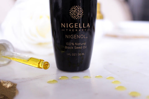 A bottle of Nigenol, 100% Natural Black Seed Oil with drops of the oil on the counter