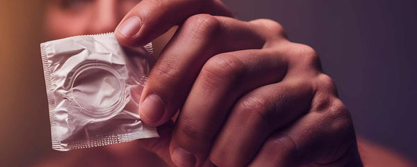 Male hand holding packaged condom (ai)