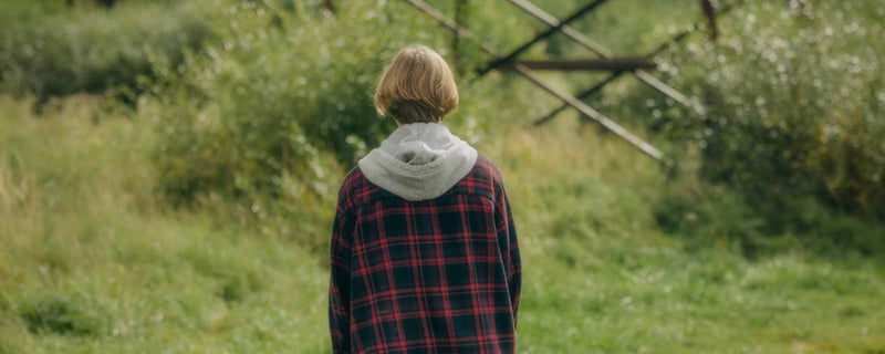 Back of person wearing plaid shirt in a green field
