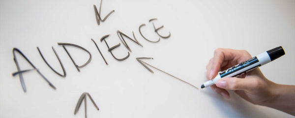 Person uses black marker to draw arrows to the word audience on a whiteboard