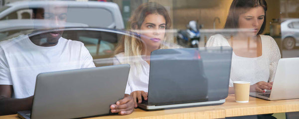 Three people working on laptop computers with window reflection