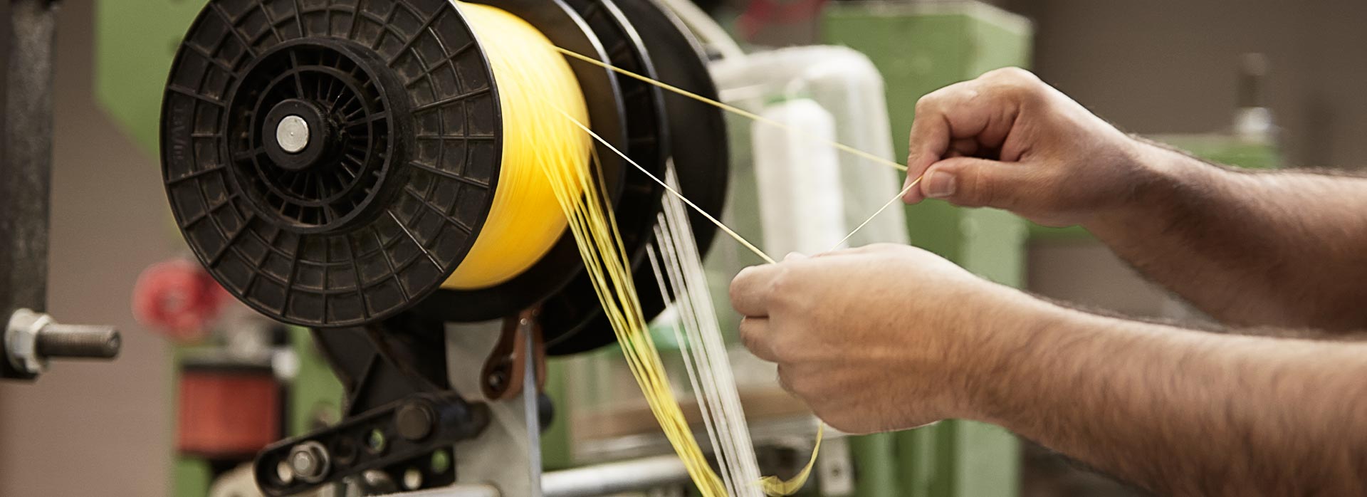 A factory workers hands winding nylon thread onto a machine.